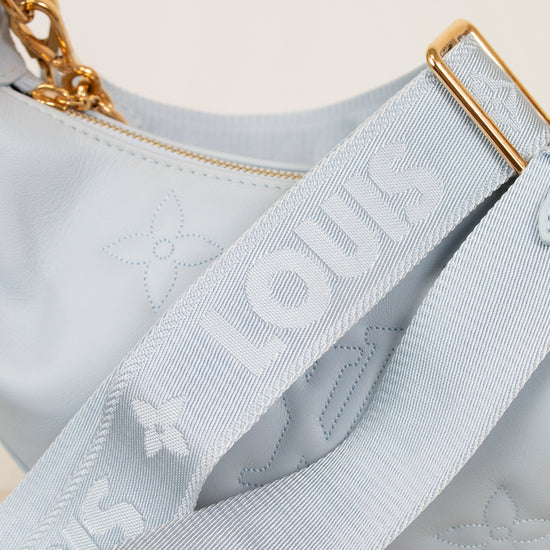 Close-up of a light blue handbag with gold chain and strap, featuring a brand logo.