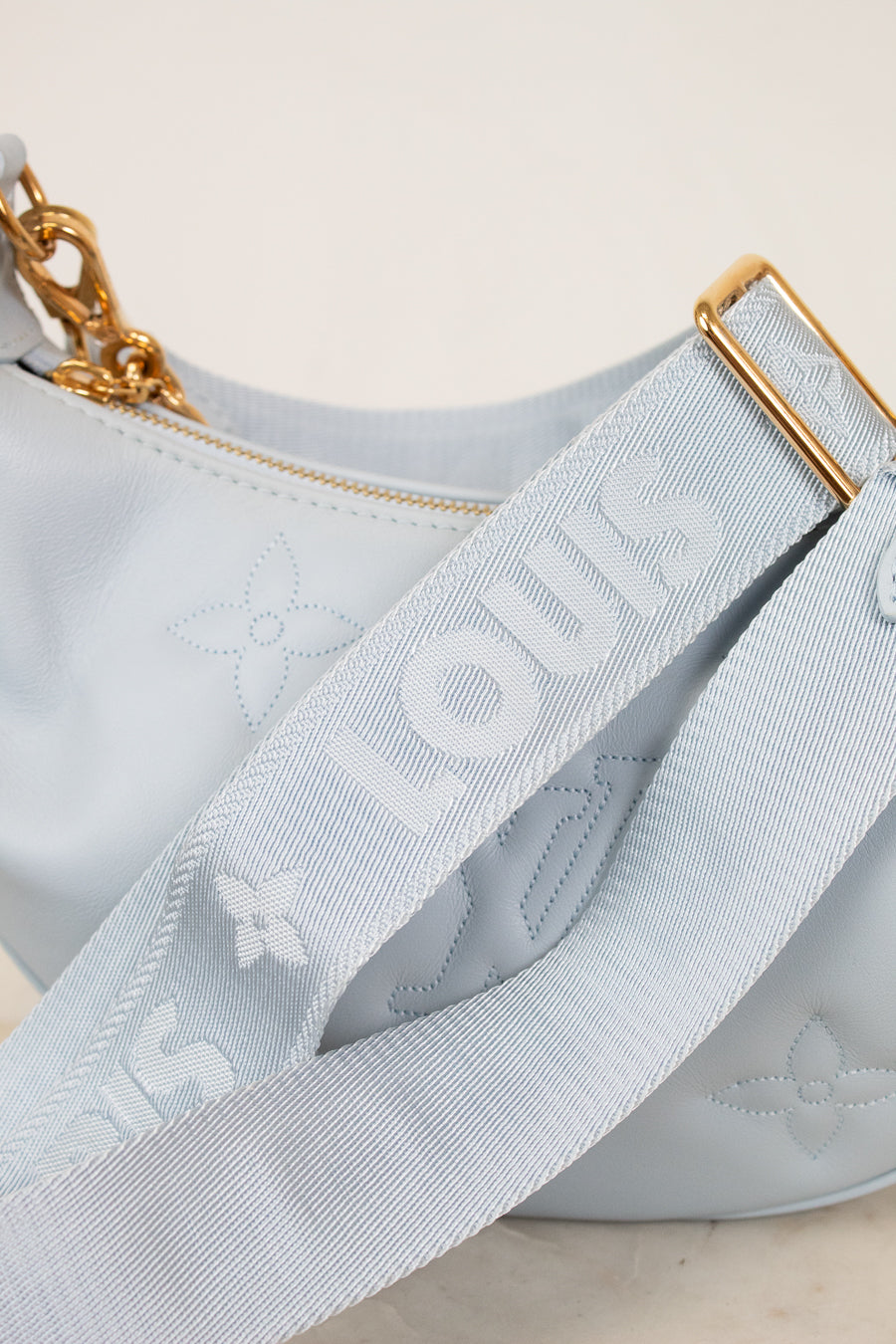 Close-up of a light blue handbag with gold chain and strap, featuring a brand logo.