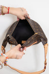 A Louis Vuitton monogram shoulder bag in brown coated canvas with tan leather trim, shown open with a person's hands holding it against a plain white background.