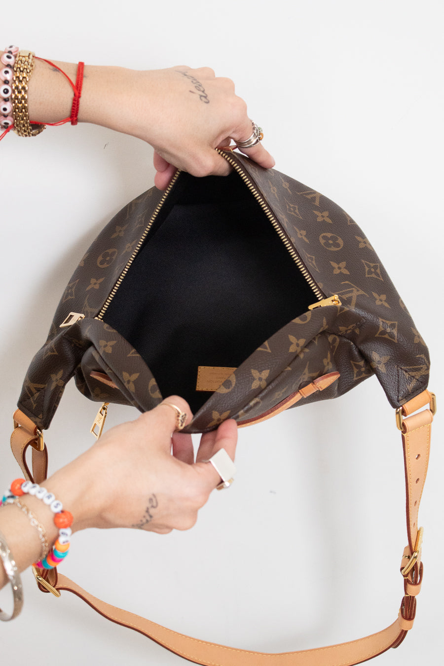 A Louis Vuitton monogram shoulder bag in brown coated canvas with tan leather trim, shown open with a person's hands holding it against a plain white background.