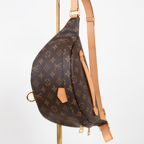 Louis Vuitton monogram bum bag in brown coated canvas with tan leather trim, displayed on a gold metal stand against a white background.