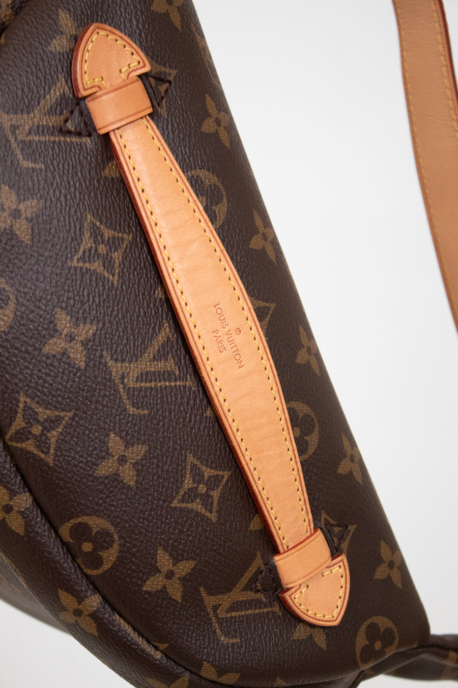 Close-up of a Louis Vuitton monogram shoulder bag in dark brown coated canvas with tan leather trim and strap, showing the classic LV monogram pattern and embossed brand text on the leather tab.