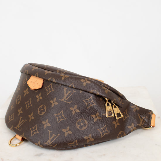 A Louis Vuitton monogram canvas fanny pack with gold-tone hardware, resting on a white marble surface against a white background.