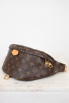 A Louis Vuitton monogram canvas fanny pack with gold-tone hardware, resting on a white marble surface against a white background.