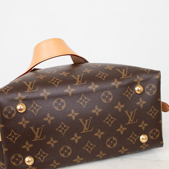 A Louis Vuitton monogram canvas handbag shown from a side angle on a light marble surface against a white background.