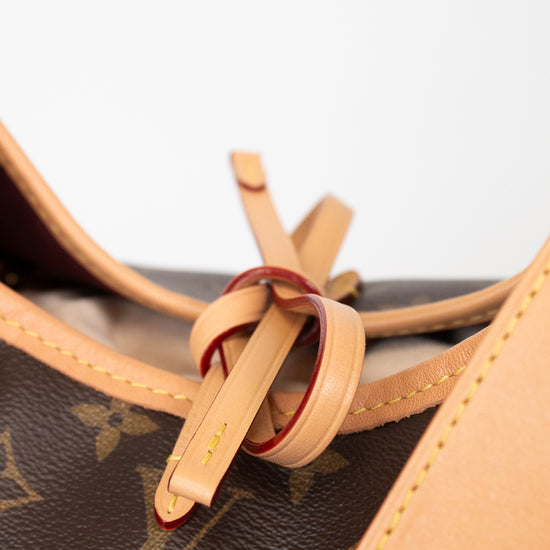 Close-up of a Louis Vuitton monogram canvas bag with tan leather trim and a decorative leather loop detail on a white background.