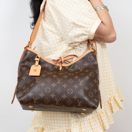 A woman wearing a yellow and white gingham dress carries a Louis Vuitton brown monogram shoulder bag with tan leather trim and strap.