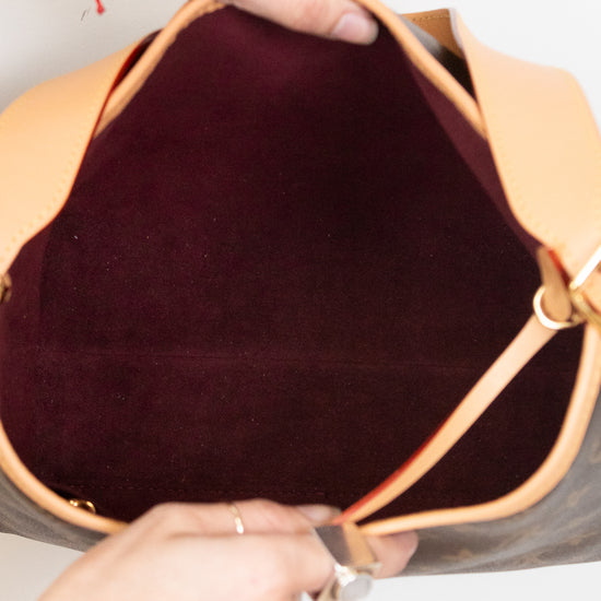 Close-up of a handbag interior with a tan leather rim and a dark burgundy velvet lining, held open by two hands wearing rings and bracelets.