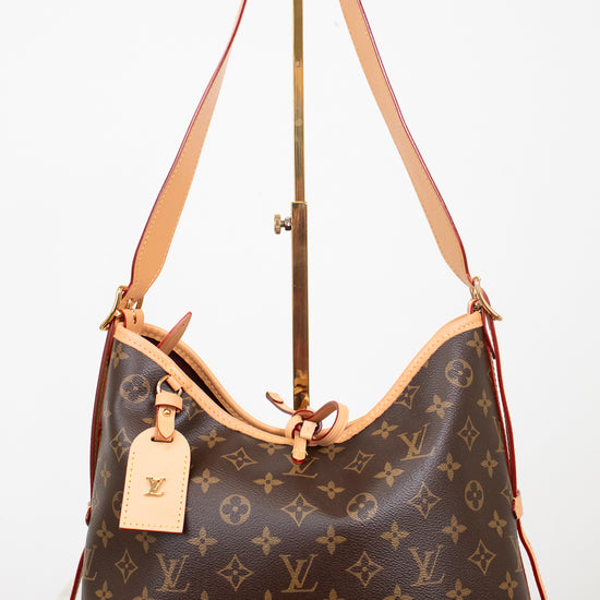 Louis Vuitton monogram canvas shoulder bag with tan leather trim and strap, displayed on a stand against a white background.