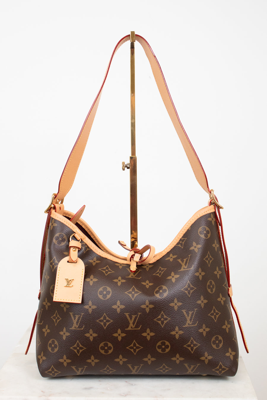 Louis Vuitton monogram canvas shoulder bag with tan leather trim and strap, displayed on a stand against a white background.