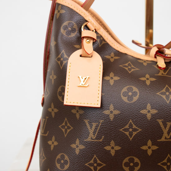 A close-up of a Louis Vuitton handbag in brown monogram canvas with light tan leather trim and a matching luggage tag featuring a gold-tone LV logo.