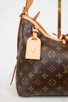 A close-up of a Louis Vuitton handbag in brown monogram canvas with light tan leather trim and a matching luggage tag featuring a gold-tone LV logo.