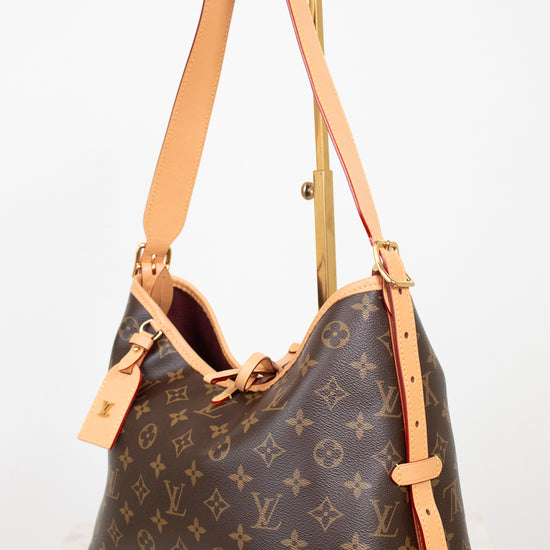 Louis Vuitton monogram canvas shoulder bag with tan leather trim and strap, displayed on a stand against a white background.