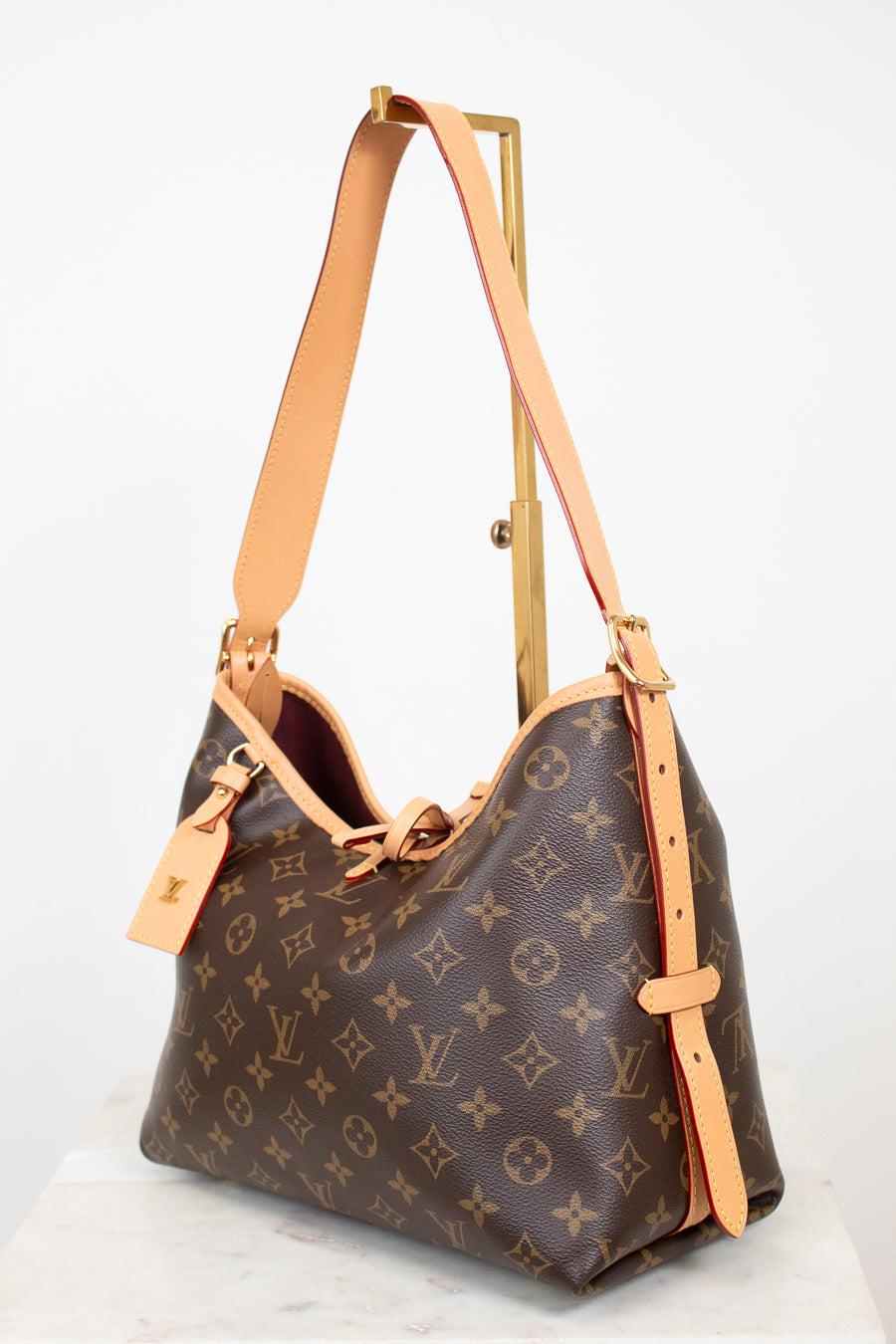 Louis Vuitton monogram canvas shoulder bag with tan leather trim and strap, displayed on a stand against a white background.