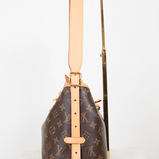Louis Vuitton monogram canvas shoulder bag with tan leather trim and strap, displayed upright on a gold stand against a white background.
