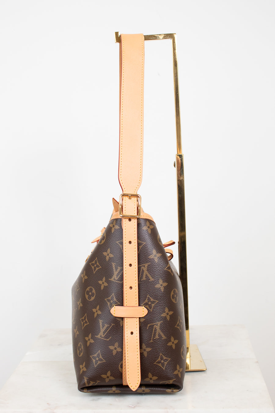 Louis Vuitton monogram canvas shoulder bag with tan leather trim and strap, displayed upright on a gold stand against a white background.
