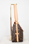 A Louis Vuitton monogram bucket bag in brown coated canvas with tan leather trim and strap, displayed upright on a gold stand against a white background.