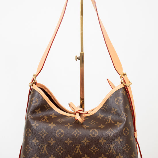 Louis Vuitton monogram canvas shoulder bag with tan leather trim and strap, displayed on a stand against a white background.