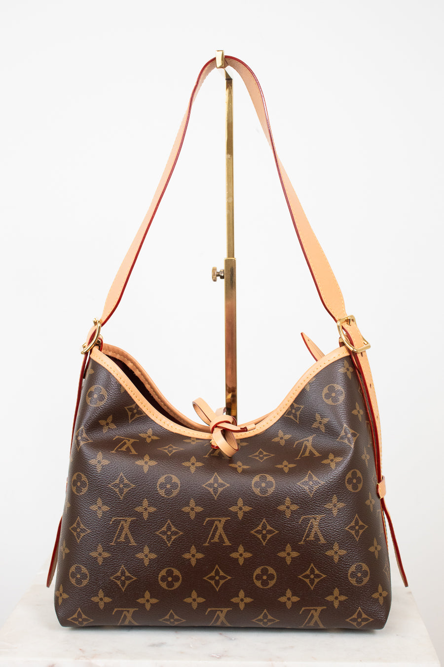 Louis Vuitton monogram canvas shoulder bag with tan leather trim and strap, displayed on a stand against a white background.