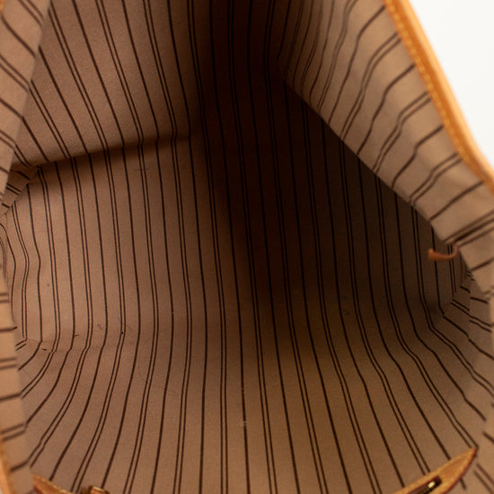 Close-up of the interior lining of a tan tote bag with thin vertical black pinstripes and a tan leather and gold-tone zipper.