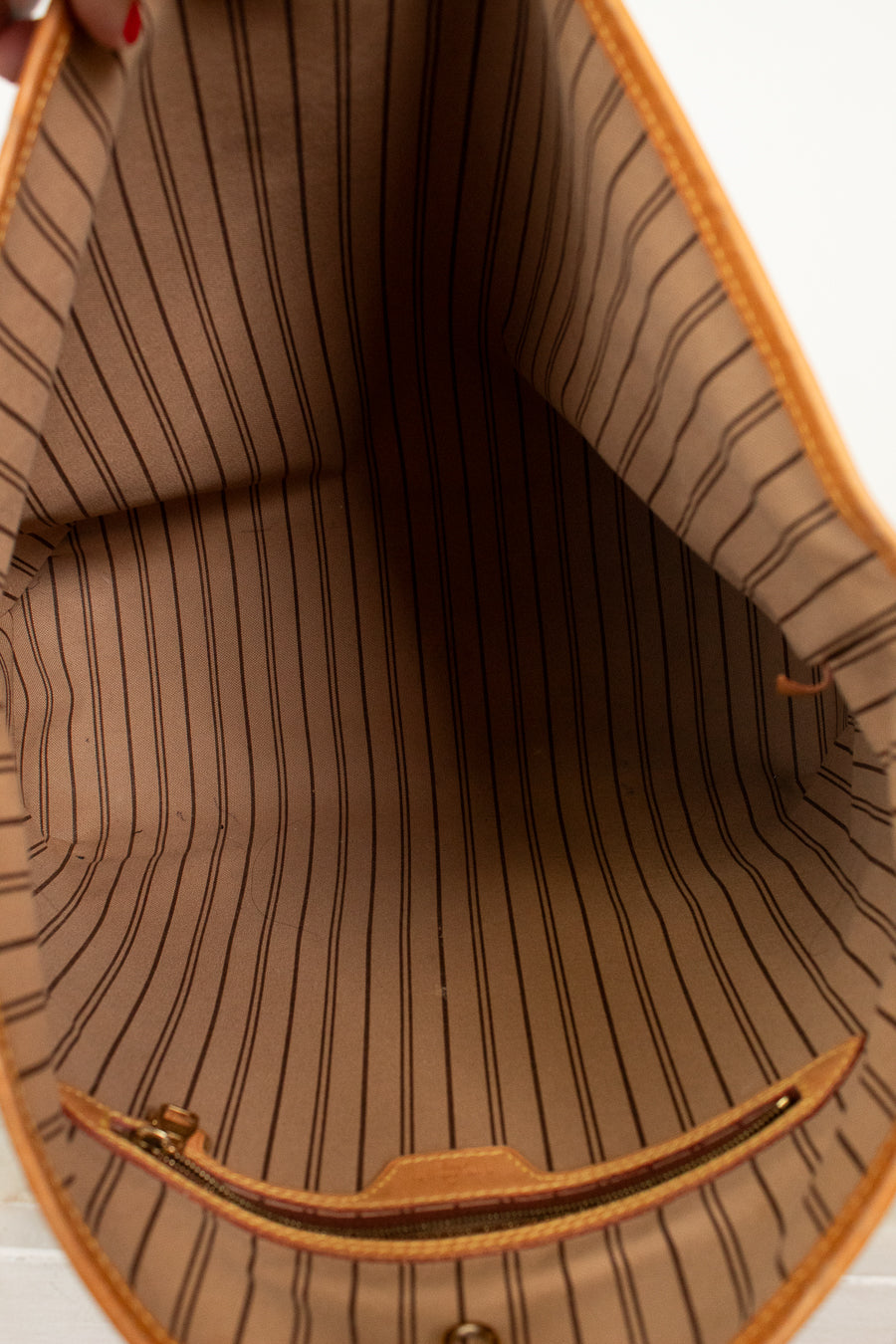 Close-up of the interior lining of a tan tote bag with thin vertical black pinstripes and a tan leather and gold-tone zipper.