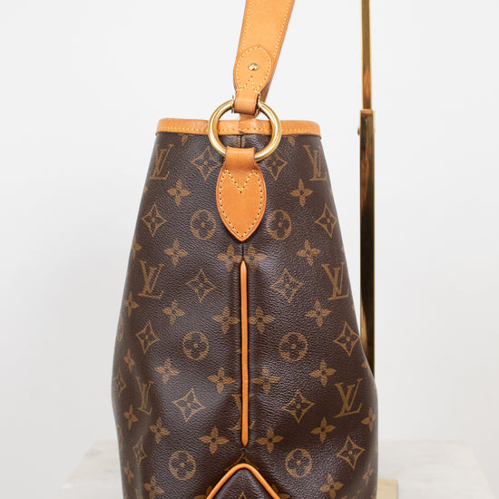 Louis Vuitton monogram coated canvas shoulder bag with tan leather trim and a gold-tone metal ring detail, displayed on a white marble surface with a gold stand against a white background.