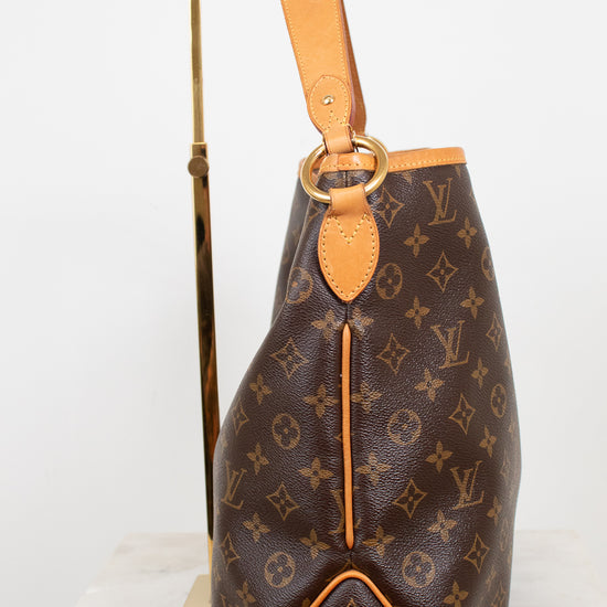 Louis Vuitton monogram canvas shoulder bag in brown with tan leather trim and strap, displayed on a gold stand against a white background.