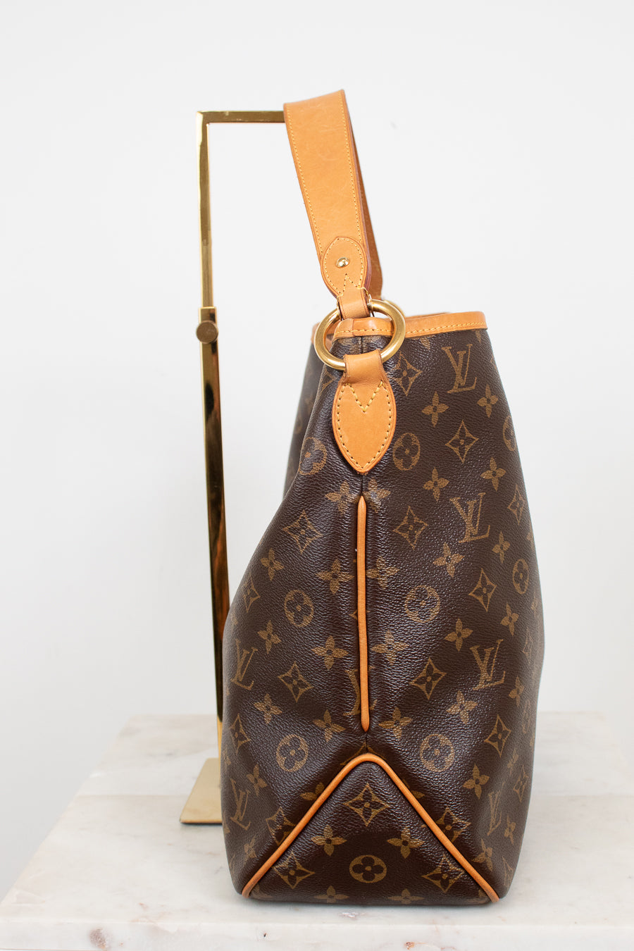 Louis Vuitton monogram canvas shoulder bag in brown with tan leather trim and strap, displayed on a gold stand against a white background.