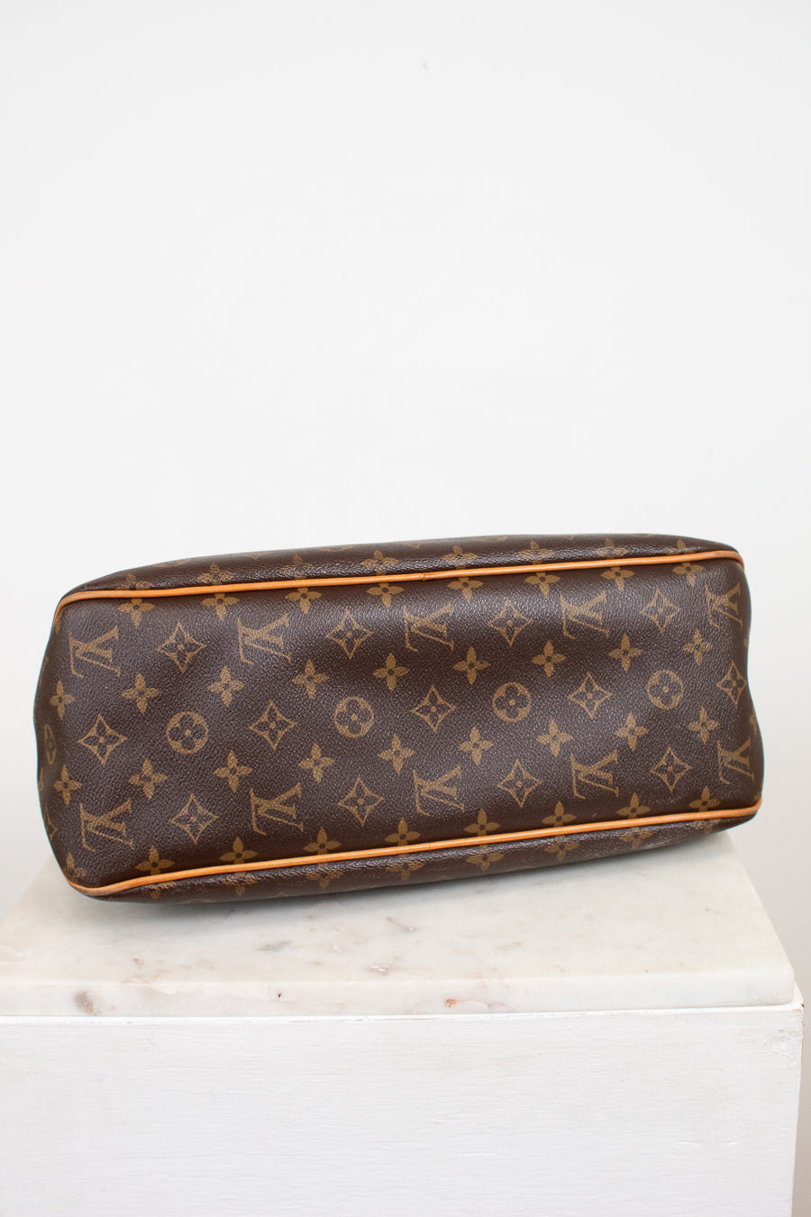 A Louis Vuitton monogram coated canvas bottom view of bag, resting on a white marble block against a white background