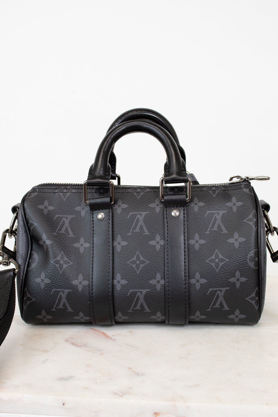 Black handbag with monogram pattern on a white marble surface