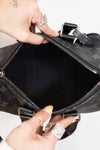 Close-up of a black handbag with a person's hands opening it on a light gray background