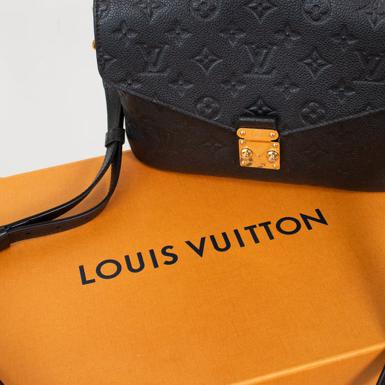 Louis Vuitton black monogram handbag resting on an orange Louis Vuitton dust bag against a white background.
