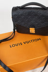 Louis Vuitton black monogram handbag resting on an orange Louis Vuitton dust bag against a white background.