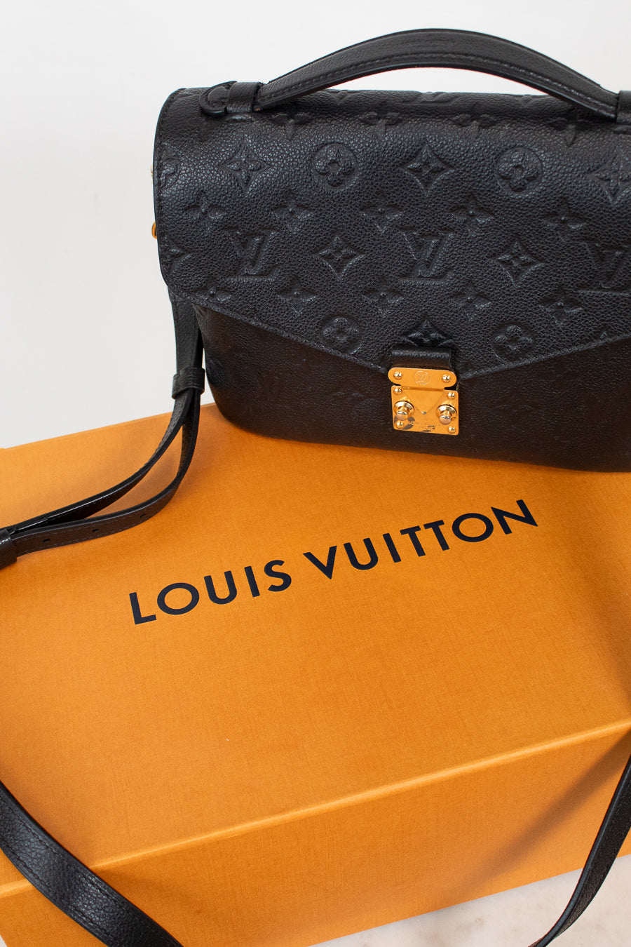 Louis Vuitton black monogram handbag resting on an orange Louis Vuitton dust bag against a white background.