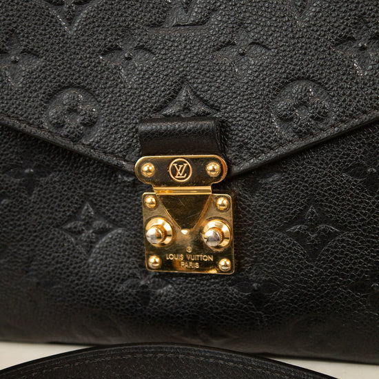 Close-up of a black Louis Vuitton monogram bag with a gold-tone closure  lock and strap on a light marble surface.