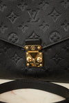 Close-up of a black Louis Vuitton monogram bag with a gold-tone closure  lock and strap on a light marble surface.