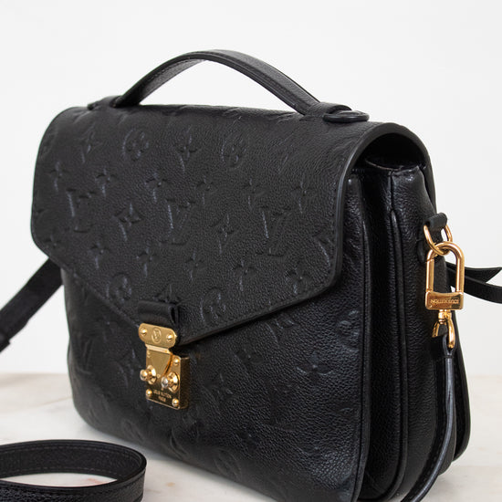 A black embossed leather handbag with a top handle, gold-tone clasp, and matching shoulder strap, photographed on a light neutral background.