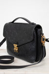 A black embossed leather handbag with a top handle, gold-tone clasp, and matching shoulder strap, photographed on a light neutral background.