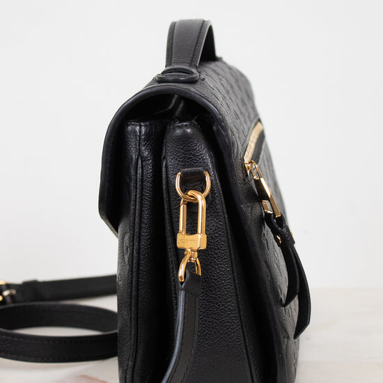 A black textured leather shoulder bag shown from a side profile view, featuring gold-tone hardware and a matching black strap on a light marble surface against a white background.