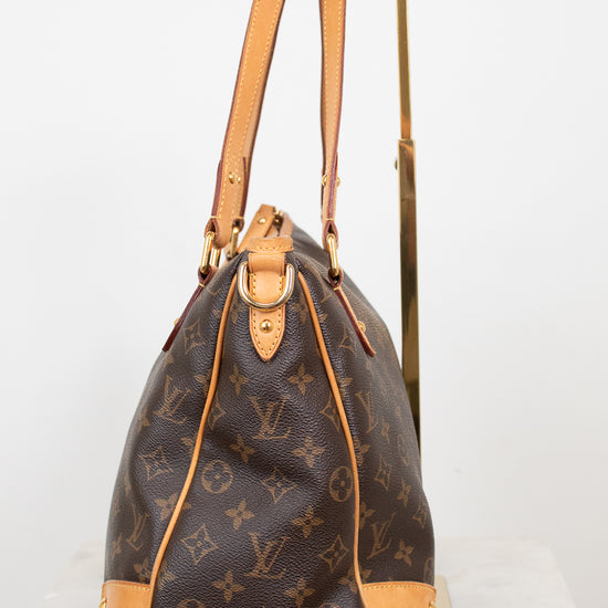 A Louis Vuitton monogram coated canvas shoulder bag with tan leather trim and gold-tone hardware, displayed on a stand against a white background.