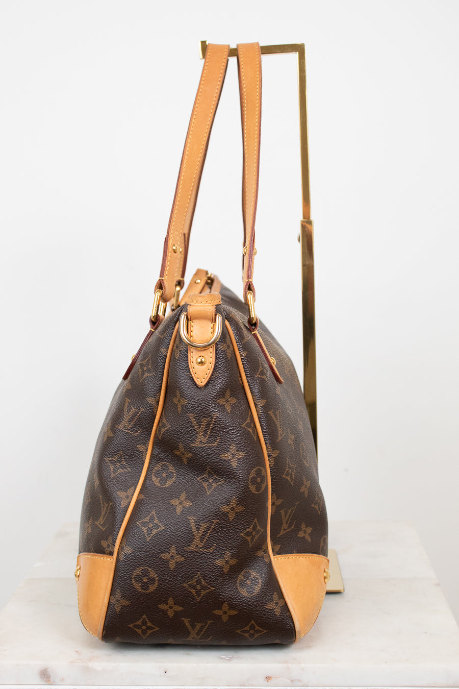 A Louis Vuitton monogram coated canvas shoulder bag with tan leather trim and gold-tone hardware, displayed on a stand against a white background.