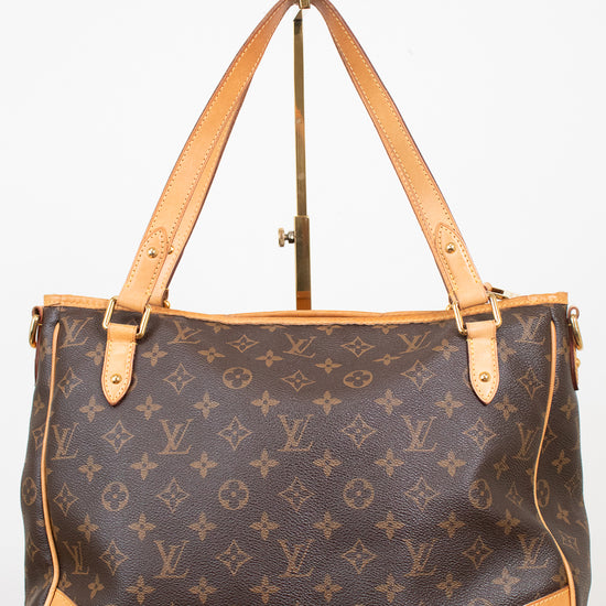 Louis Vuitton monogram canvas tote bag with tan leather handles and corner protectors, displayed on a stand against a white background.