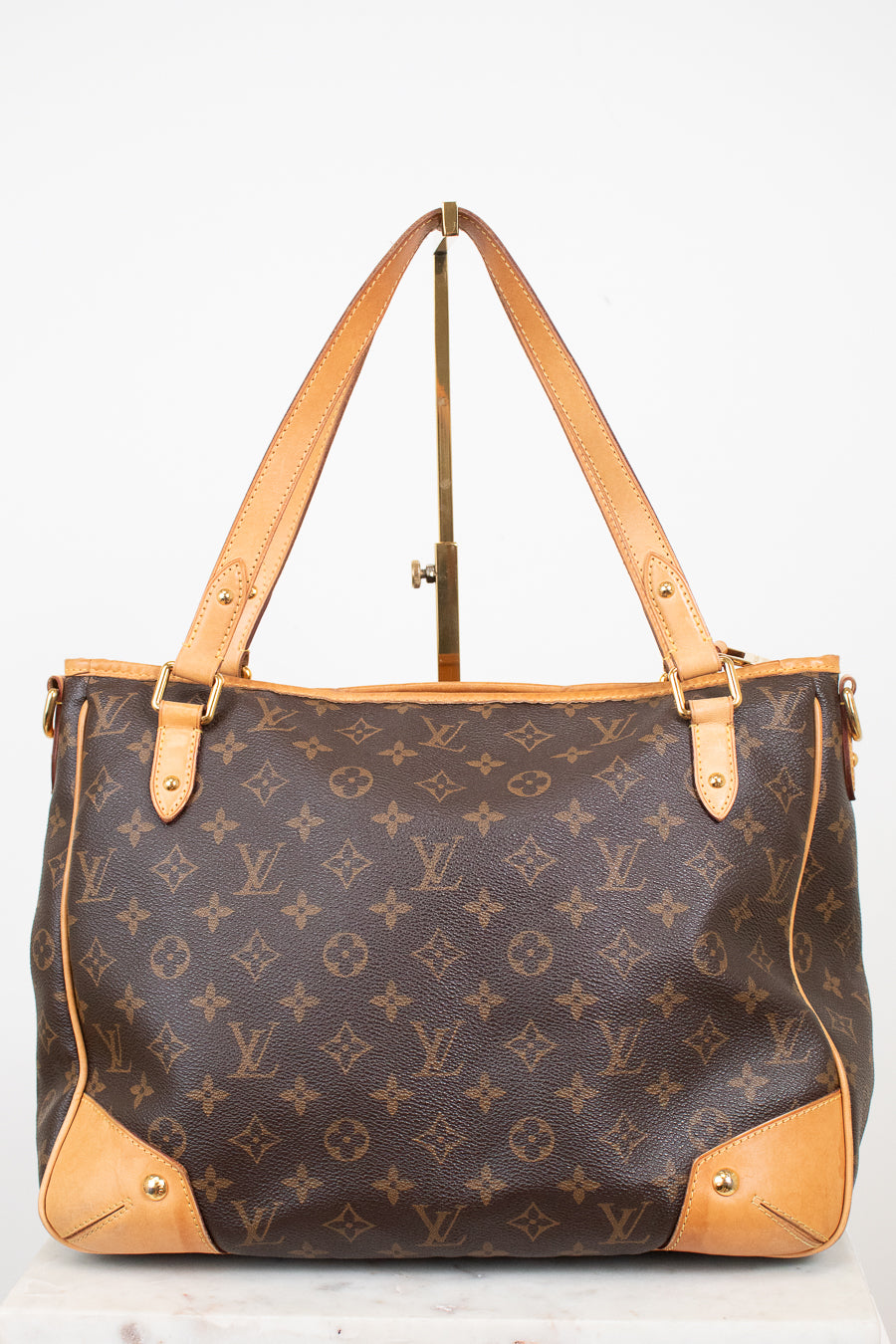 Louis Vuitton monogram canvas tote bag with tan leather handles and corner protectors, displayed on a stand against a white background.