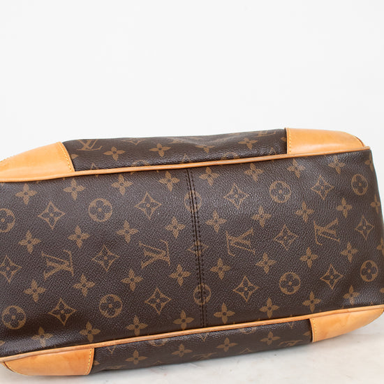 Louis Vuitton monogram coated canvas handbag shown from the bottom corner, featuring brown coated canvas with tan leather trim and corner protectors on a light marble surface.