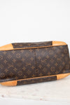 Louis Vuitton monogram coated canvas handbag shown from the bottom corner, featuring brown coated canvas with tan leather trim and corner protectors on a light marble surface.