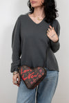 Person wearing a dark gray sweater and blue jeans, holding a heart-shaped Louis Vuitton bag.