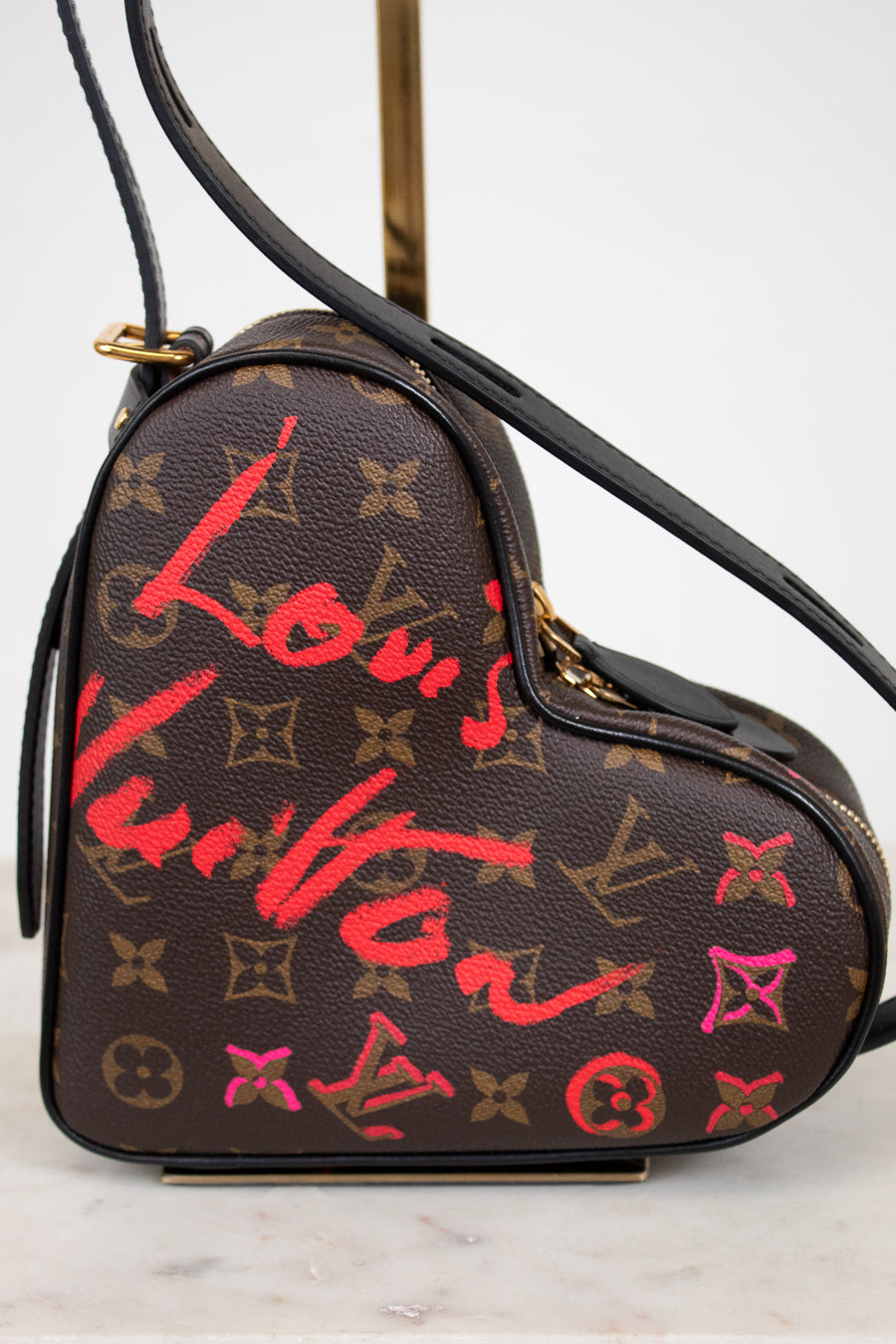 Heart-shaped Louis Vuitton bag with red and pink graffiti-style text on a white background