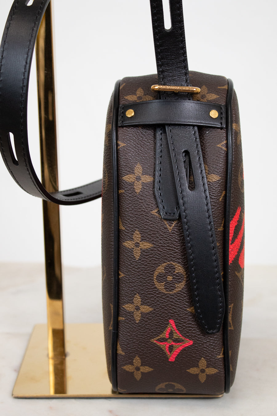 Designer handbag with monogram pattern on a stand against a white background