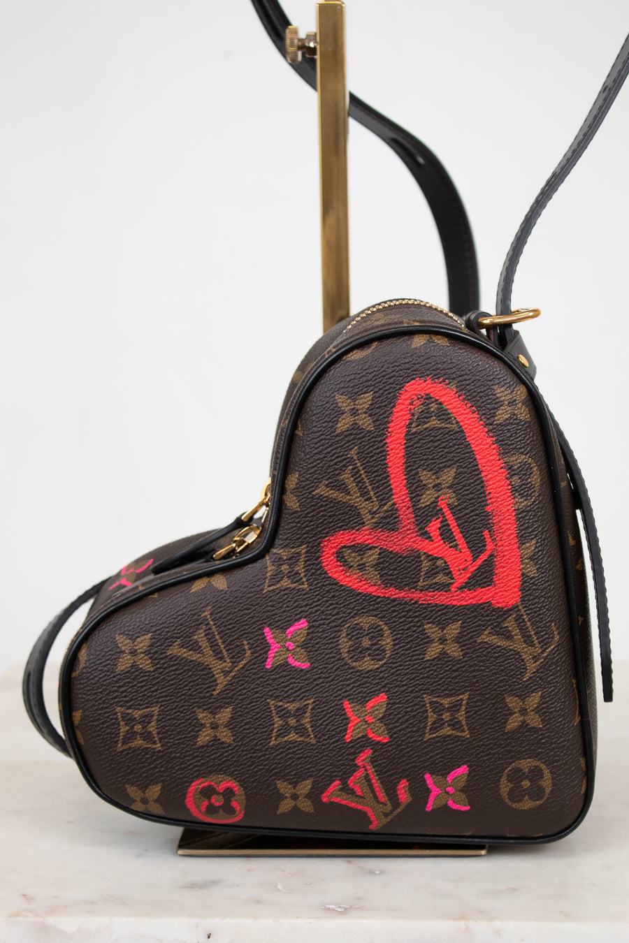 Heart-shaped handbag with monogram pattern and red heart design on a white background