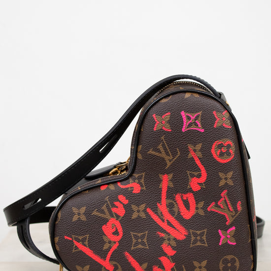 Heart-shaped handbag with Louis Vuitton monogram and graffiti-style text on a white background
